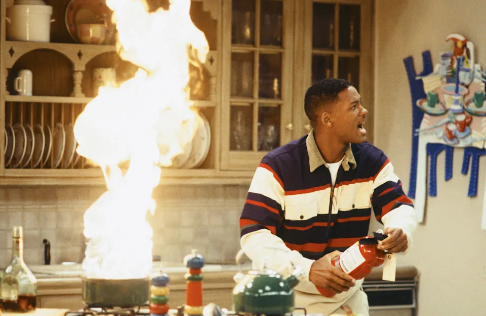 Person in a kitchen, surprised, holding a fire extinguisher near a stovetop flame