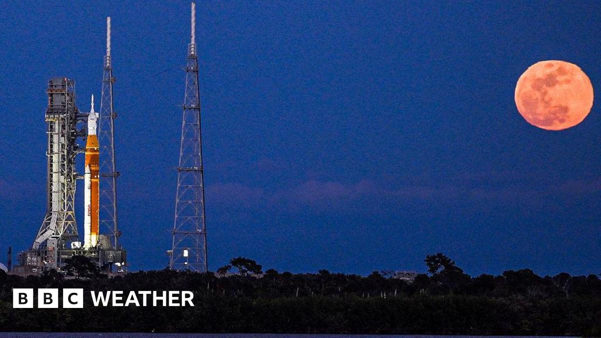Artemis II rocket on the launch pad in Cape Canaveral with a full, bright and orange Moon rising in the sky next to it