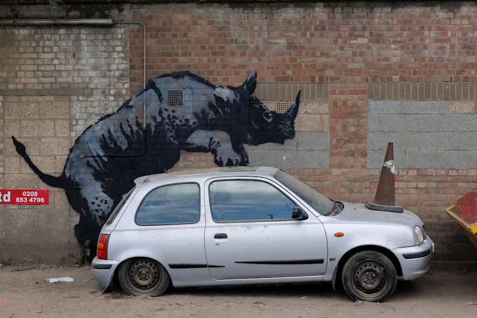 Car parked next to a wall with street art of a rhino appearing to climb over it