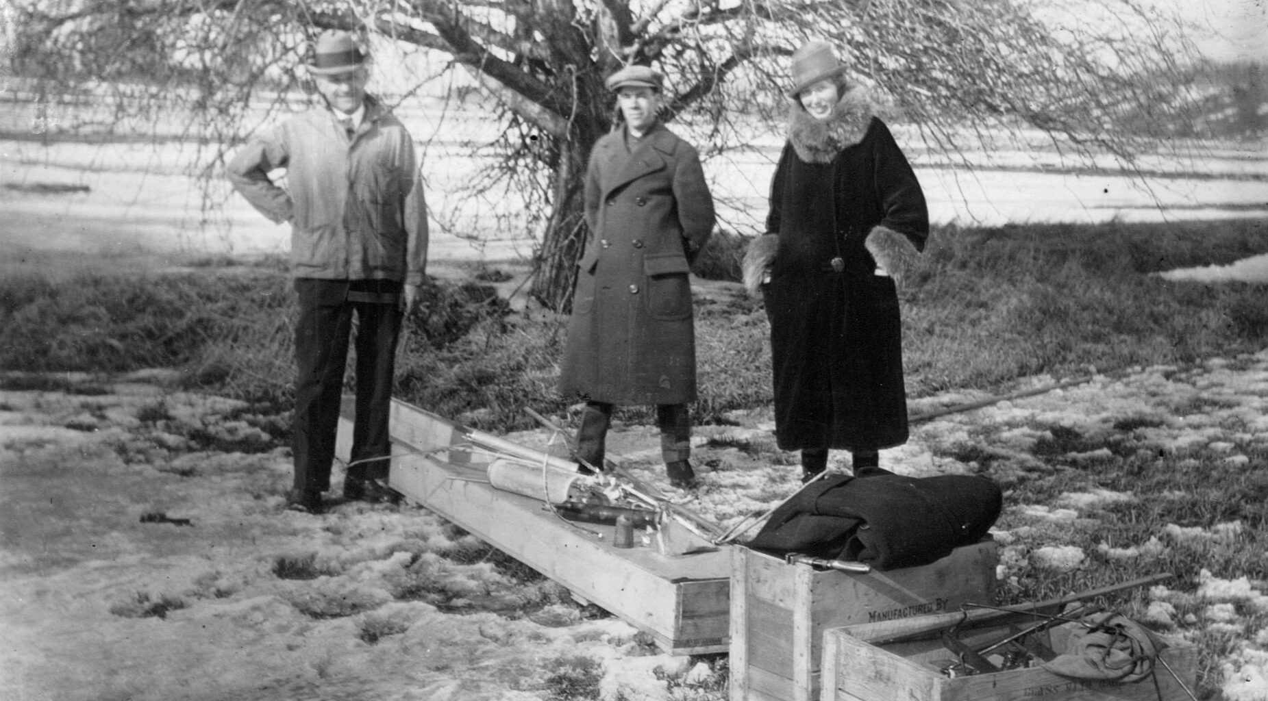 black-and-white photograph of a trio of people standing outdoors with wooden crates at their feet