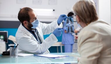 doctor holding up lung x-rays, while pointing at them with a pen and explaining them to a patient