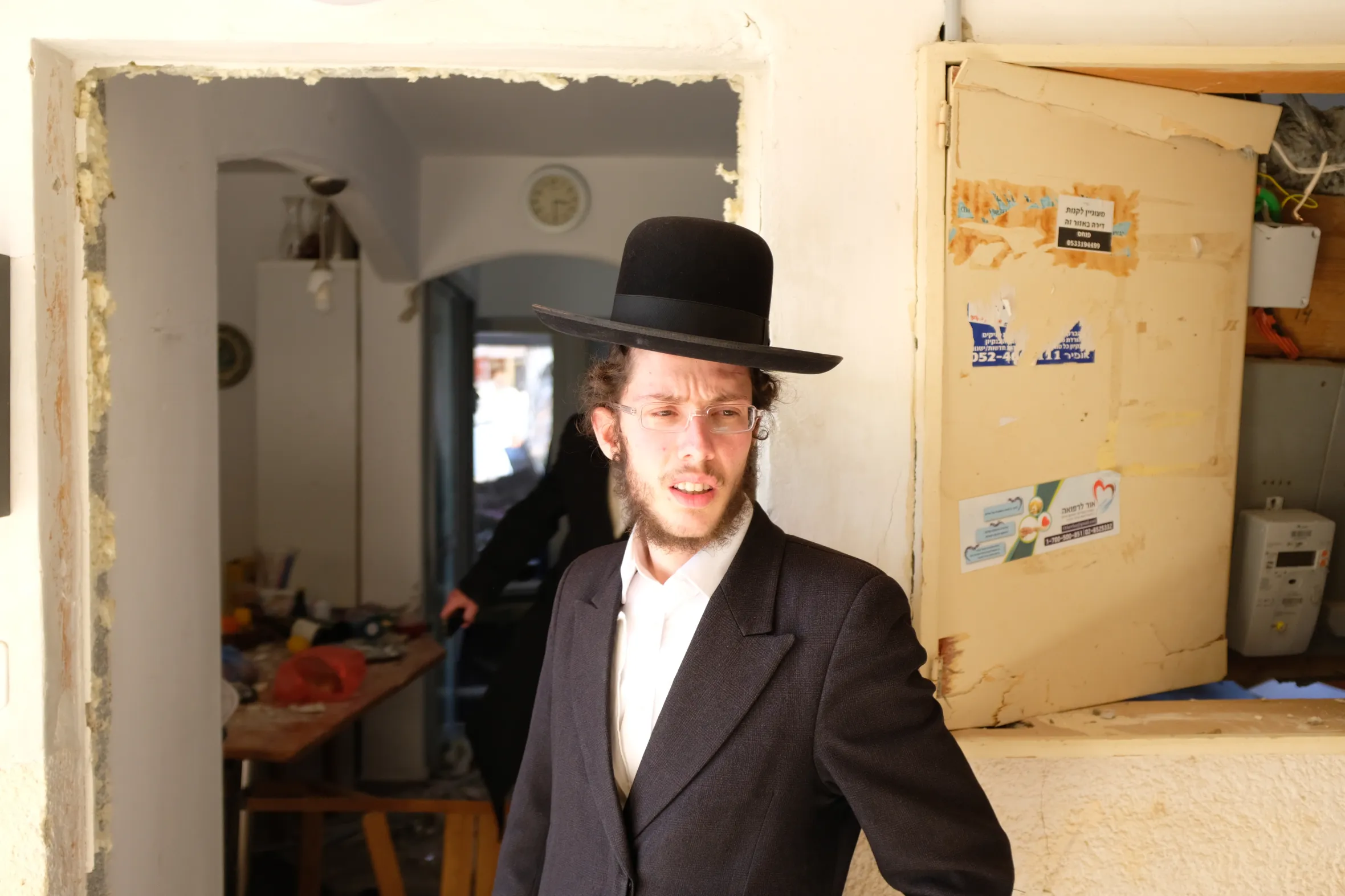 A young man named Lozor, wearing a black hat, glasses, and a suit, stands in a doorway looking into the distance.