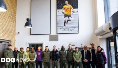 A football team posing underneath two large paintings hanging in the entrance of a building