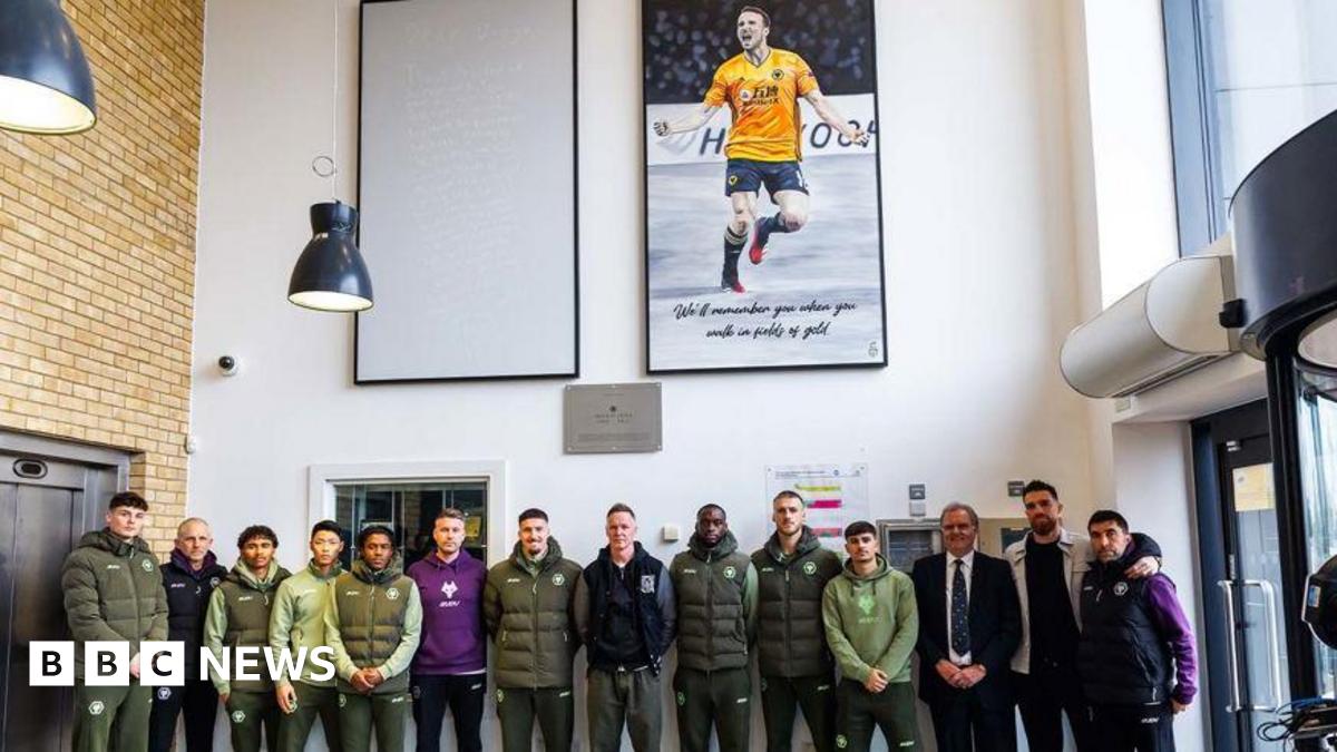 A football team posing underneath two large paintings hanging in the entrance of a building