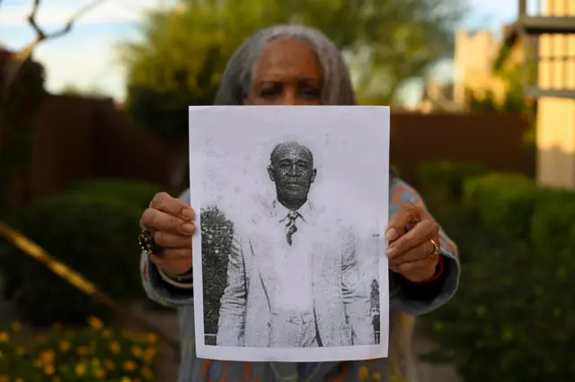 Carole Coles Henry holds a black and white photo of her great great grandfather Clem Coles as she stand for di backyard of her home in Phoenix, Arizona, US on 11 November 2022 in Phoenix, Arizona. Clem Coles bin dey enslaved on di Coles Hill Plantation in Chatham, Virginia. 