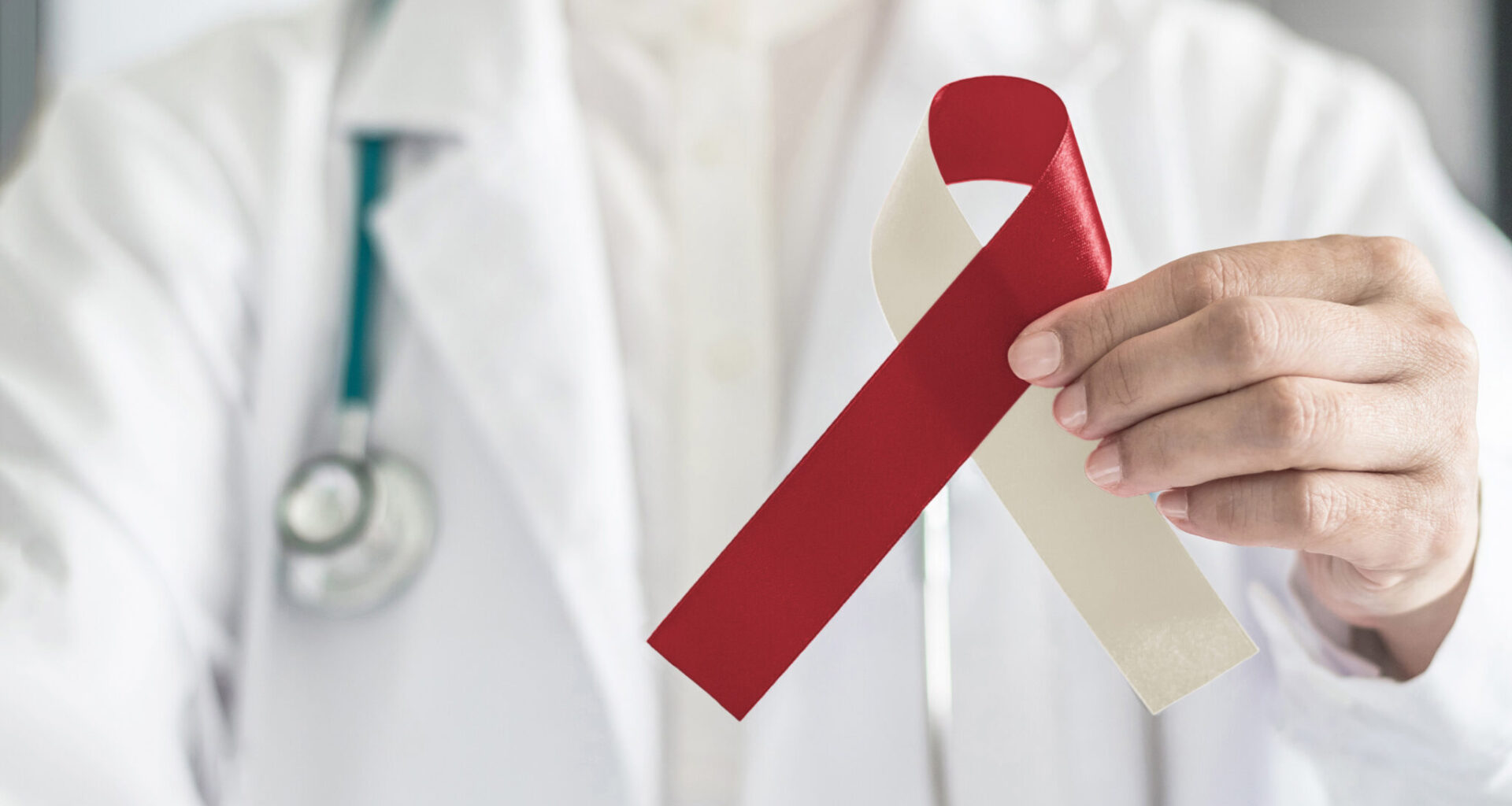 Burgundy ivory ribbon awareness on doctor's hand, symbolic bow color for head and neck cancer, oral squamous cell carcinoma, throat, laryngeal and pharyngeal cancer. (iStock)
