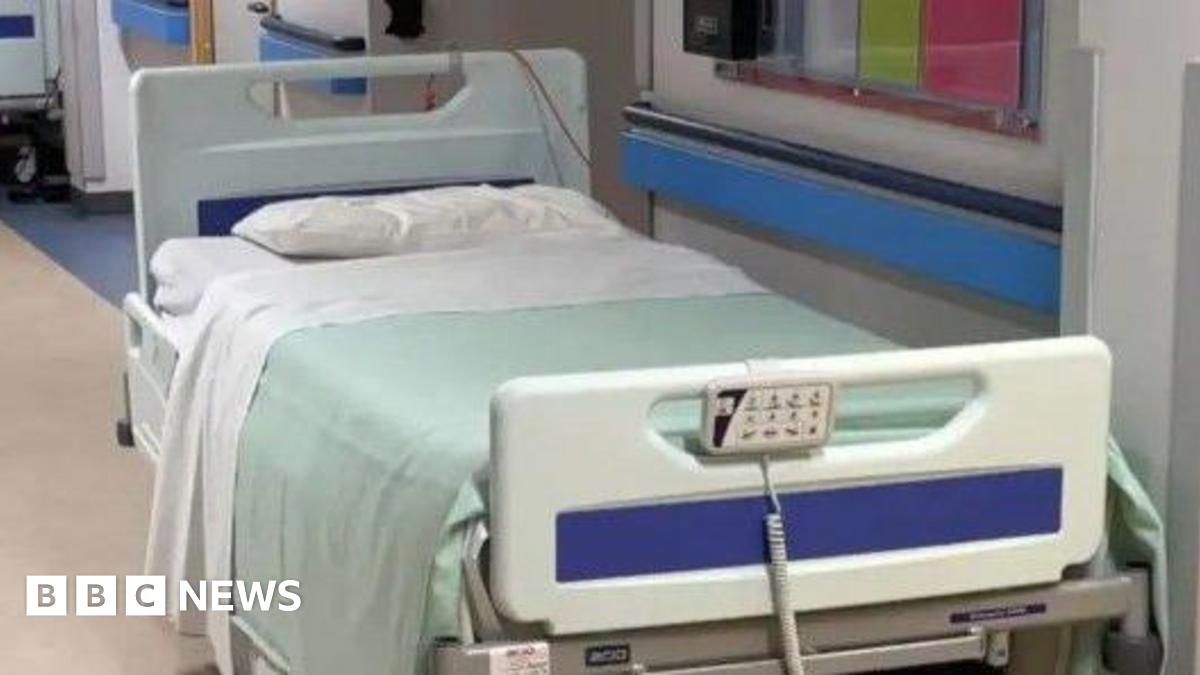 A hospital bed, which has a white pillow and sheet and a pale green blanket.