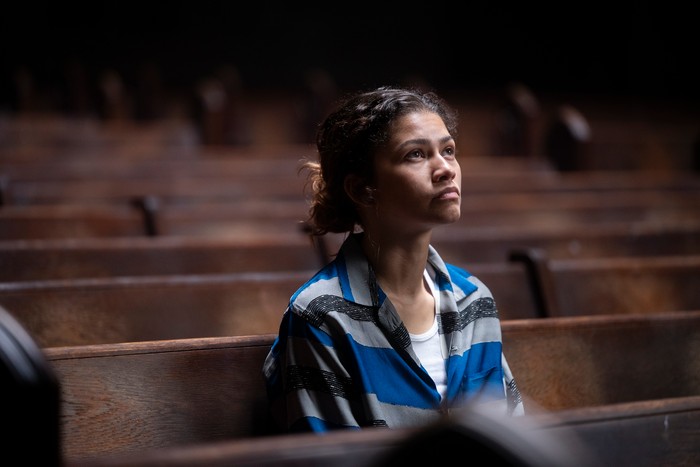 euphoria-zendaya-s3 Zendaya sitting in an auditorium, wearing a patterned shirt and looking sad, tilting her head upwards towards the sunlight.