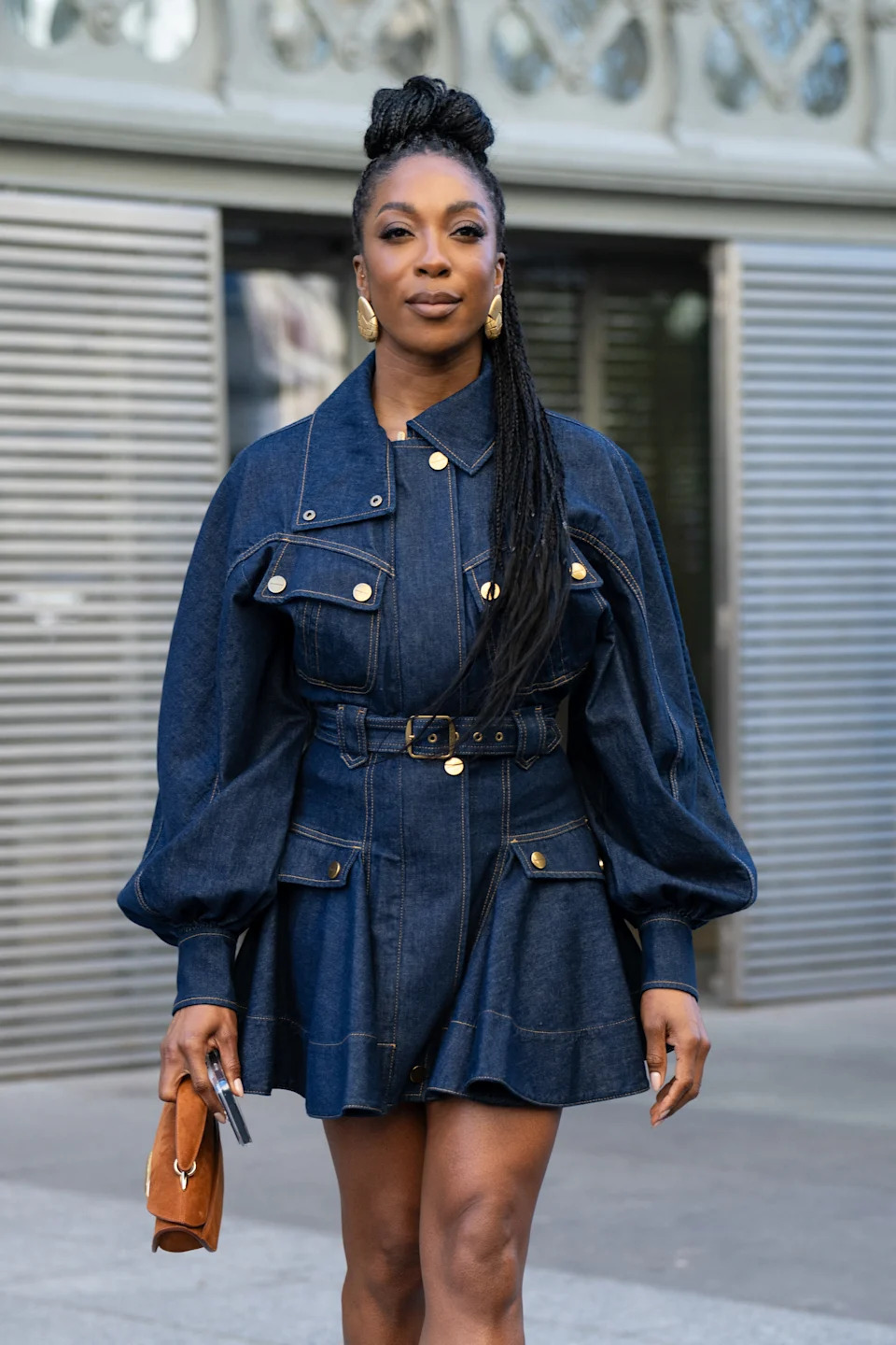 A person on the street wearing a stylish denim dress with puffed sleeves and a belted waist, holding a small clutch
