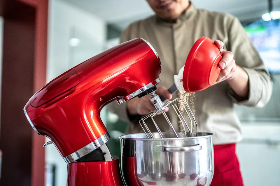 Person adds ingredients to electric mixer with whisk attachment in kitchen