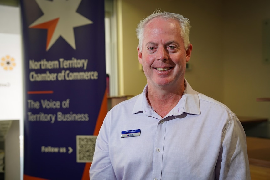 A man in a light blue shirt smiles at the camera