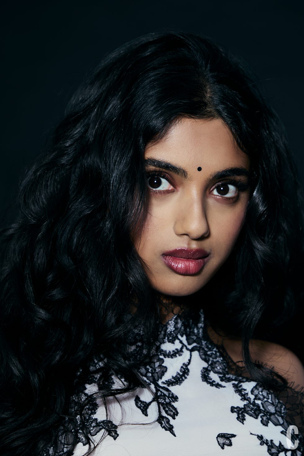 A woman with long, wavy black hair wearing a dress with lace detailing.