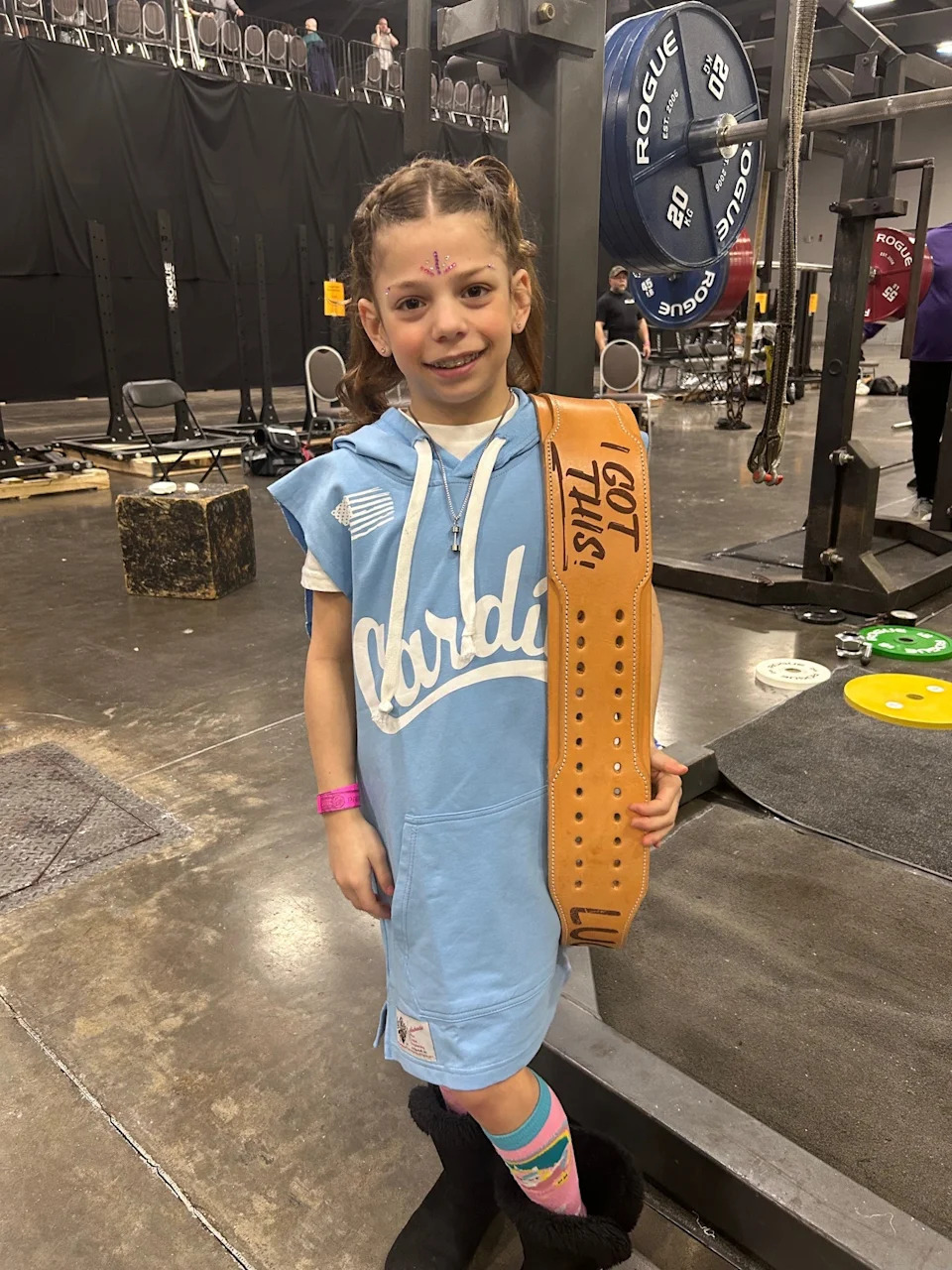 Lucy Milgrim, 9, holds a custom-made weight belt, created for her by Cardillo Weightbelts. In March 2026, a video of Milgrim deadlifting 180 pounds during a powerlifting competition went viral on social media.
