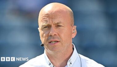 Canavan is bald and is wearing a white shirt and has a mic on.