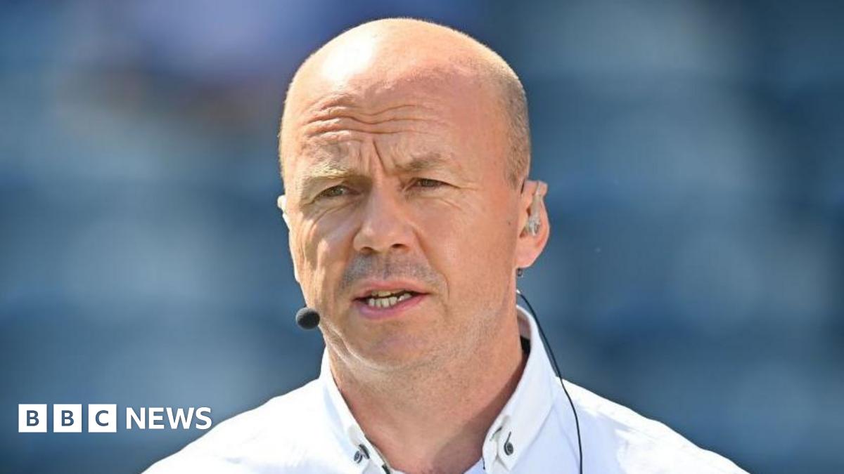 Canavan is bald and is wearing a white shirt and has a mic on.