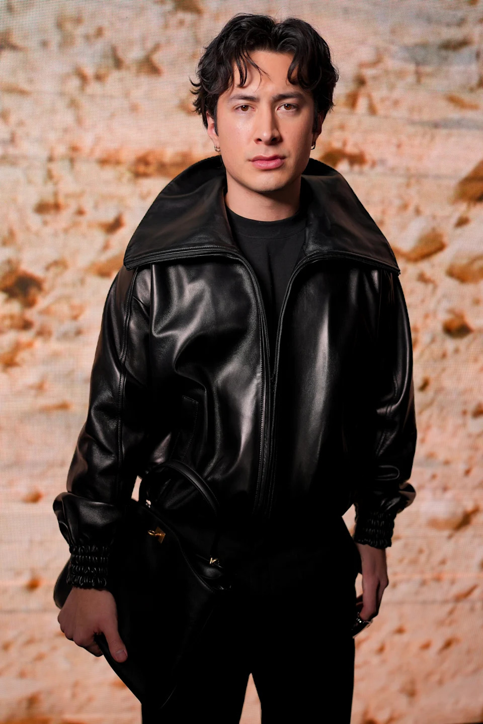 A person in a leather jacket poses confidently against a textured backdrop, suitable for a fashion-forward celebrity feature