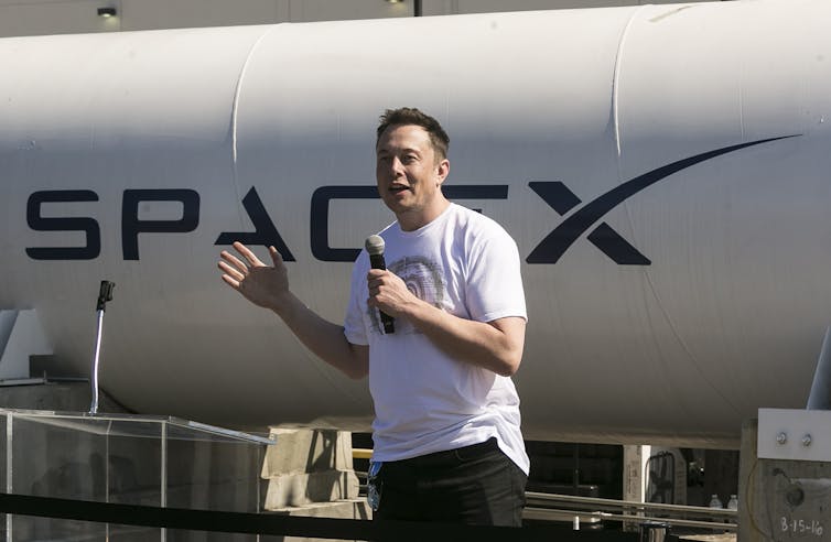 Elon Musk standing in front of a vehicle with a 'SpaceX' decal.