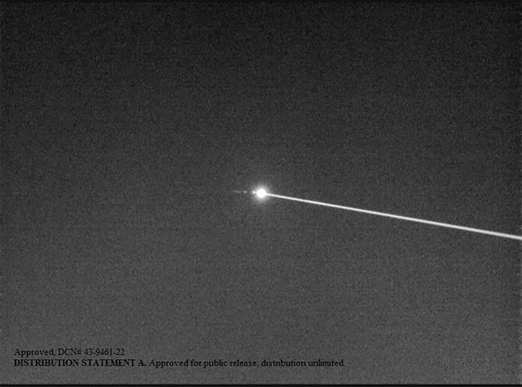 Black and white photo of a laser beam hitting a small object