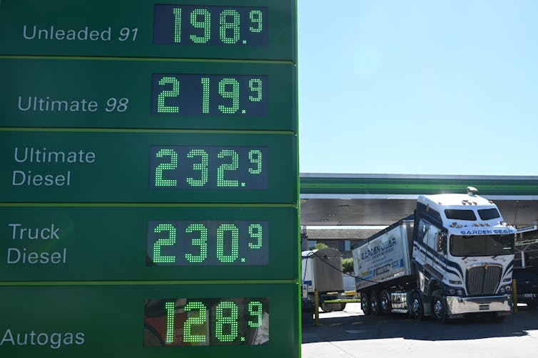 fuel prices sign in foreground at service station, with truck refuelling behind.