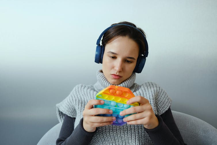 A girl wearing headphones and playing with a multicoloured bubble popper fidget toy