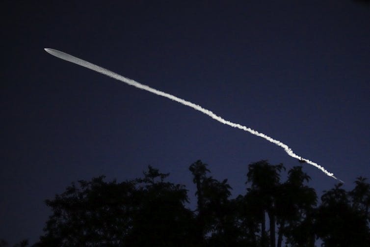 Image of a white streak across a dark sky, showing a A SpaceX Falcon 9 rocket carrying 26 Starlink satellites launched from Vandenberg Space Force Base in California.