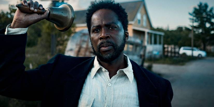 Boyd Stevens stands on the street outside a house and holds up a bell in From