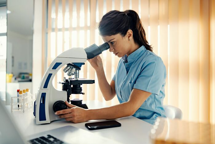 Female doctor in scrubs examining samples through a microscope revealing behind-the-scenes feelings and opinions of doctors