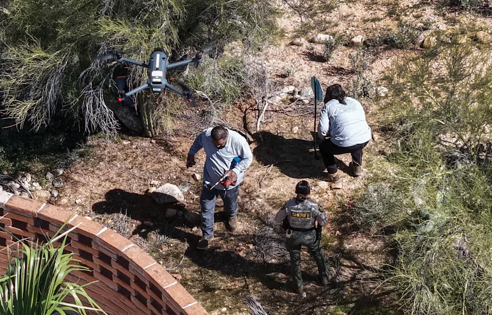 A Pima County Sheriff deputy watches as workers place "No Trespassing" signs around the home of Nancy Guthrie. 