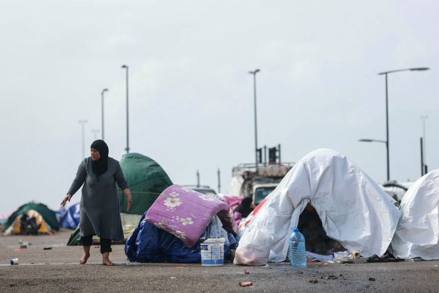 A displaced woman stands beside her tent, covered in plastic sheeting to shield them from the stormy weather along Beirut's seafront area on March 15, 2026.