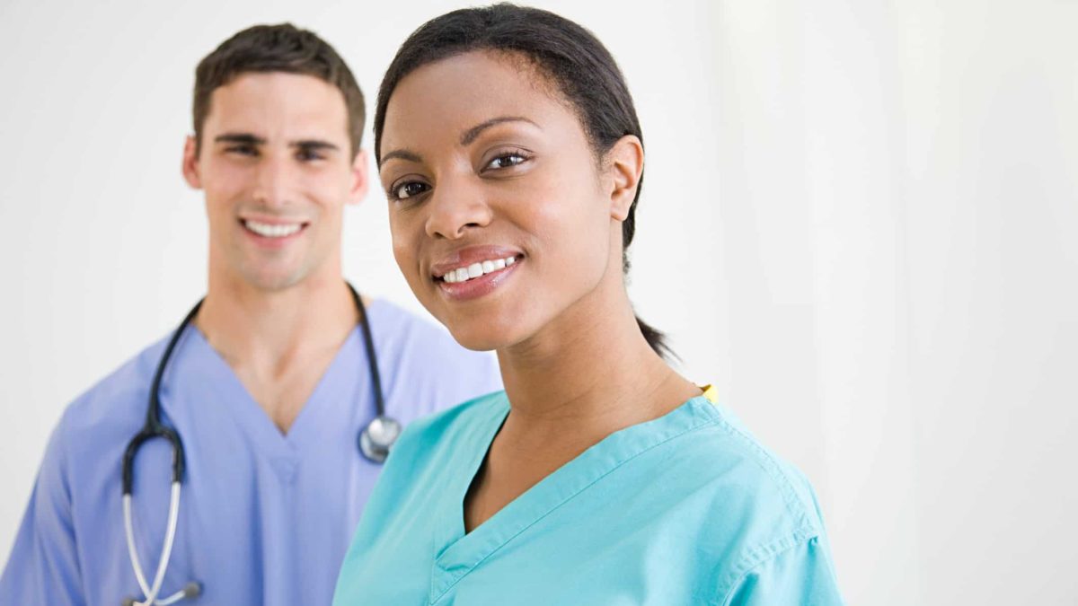 A male doctor and a woman in scrubs in the foreground smile.