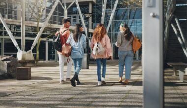 Education campus, students and walking at college to class with talking, conversation or exam chat. Back, friends and diversity outdoor at university with backpack for learning, scholarship and study
