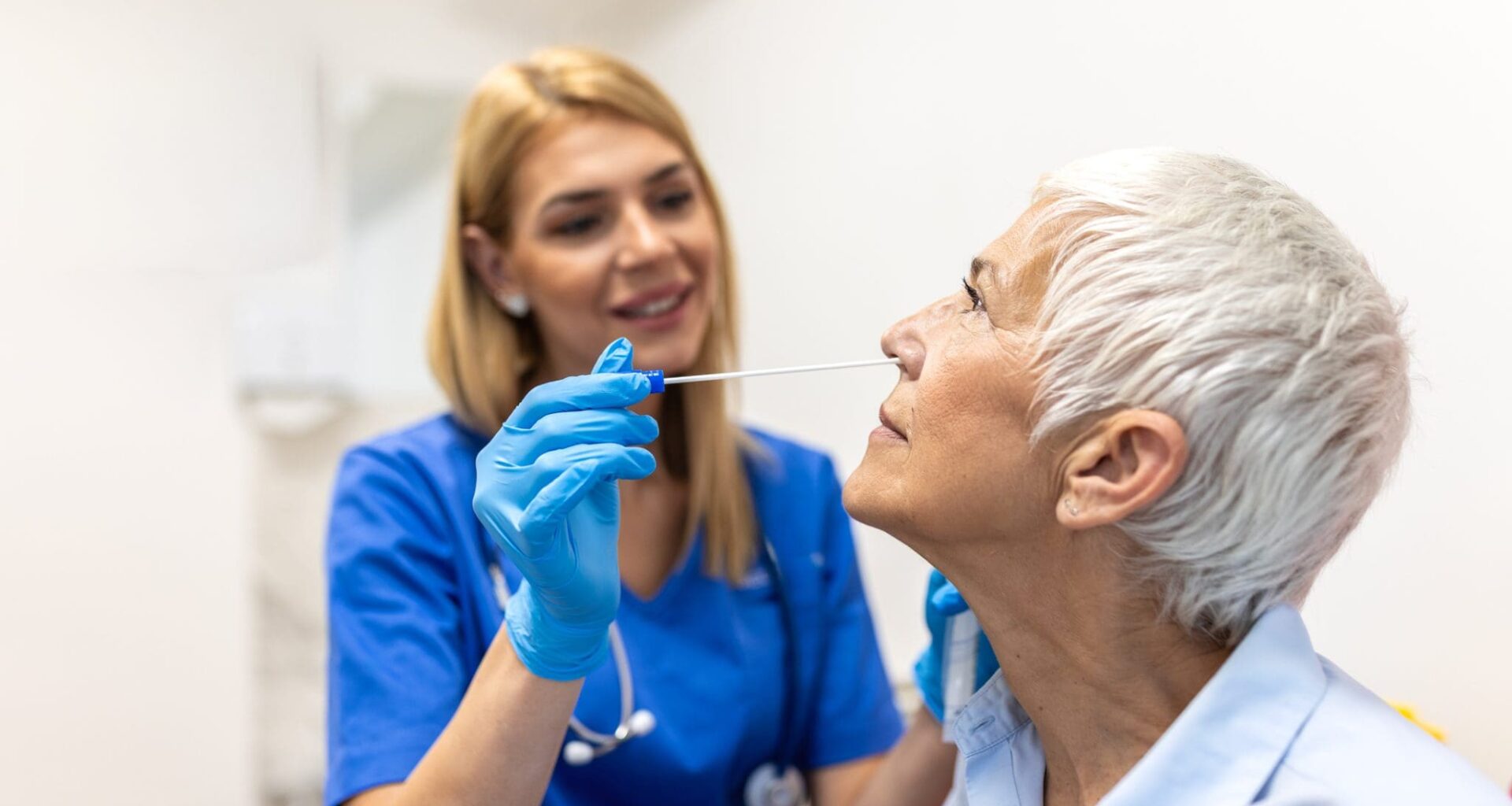 Nurse Taking Nasal Swab Test from Senior Woman in Clinic. Healthcare And Medicine concept. Professional doctor in blue gloves performing covid-19 or flu diagnostic procedure for elderly patient.