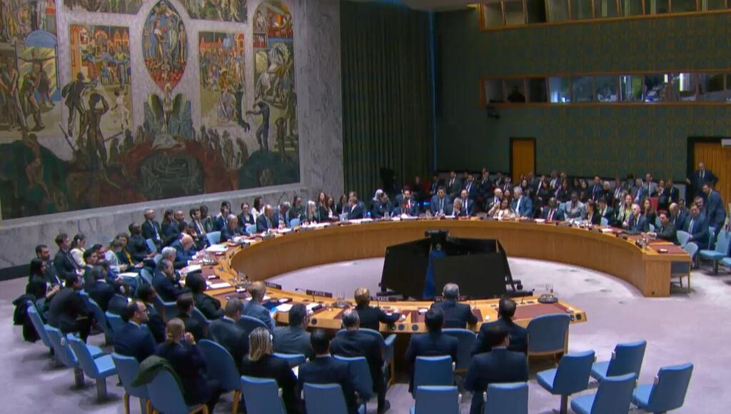 A diplomatic meeting at the United Nations Security Council with delegates seated around a large circular table.