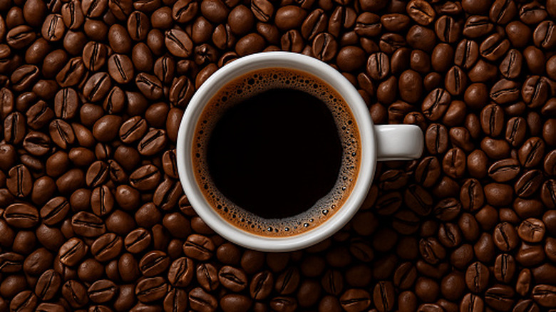 Top view of white coffee cup full of black coffee, surrounded by whole coffee beans