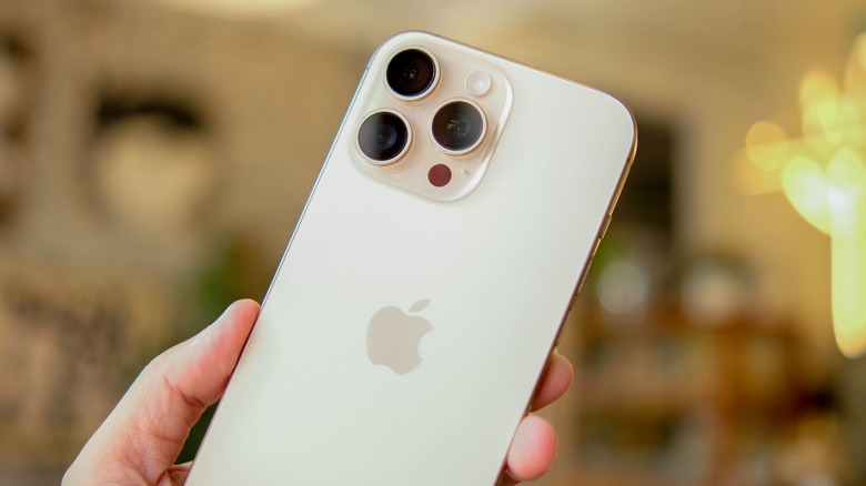 An individual holding a white iPhone in their hand, the background is blurred heavily but may be a room in an individual's house