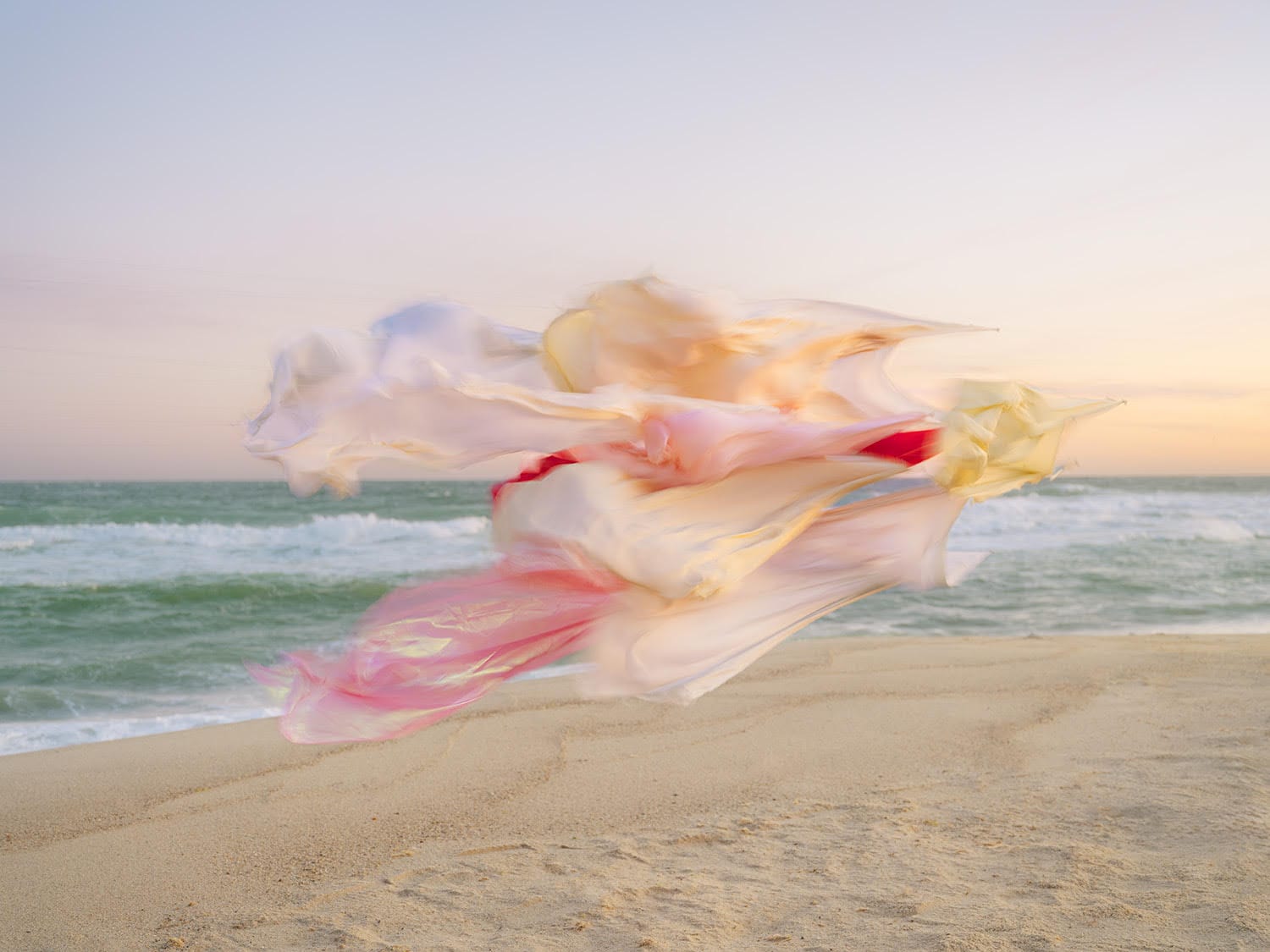 A photograph by Thomas Jackson of numerous pieces of colorful fabric that are seemingly suspended in the air on a beach