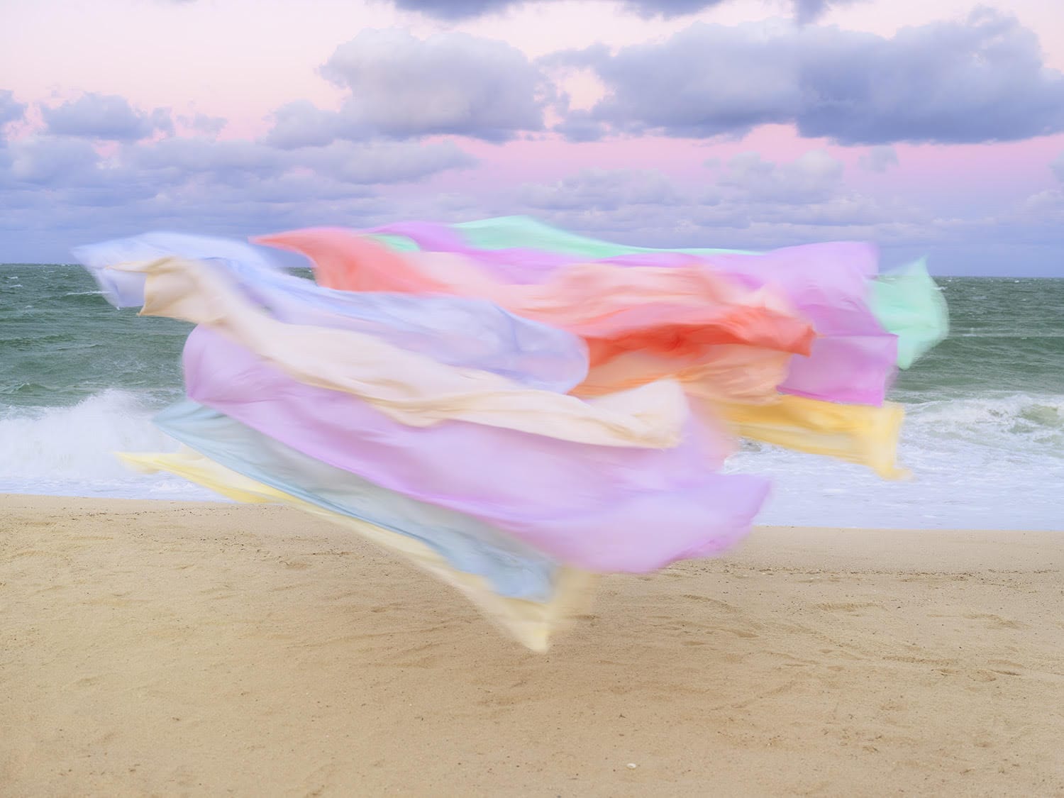 A photograph by Thomas Jackson of numerous pieces of colorful fabric that are seemingly suspended in the air on a beach