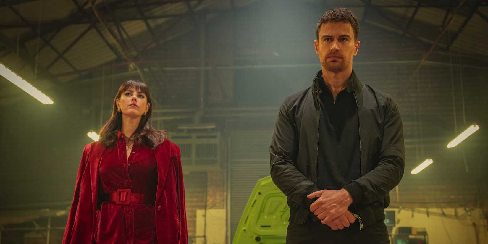 Kaya Scodelario as Susie and Theo James as Eddie stand together in a hangar in The Gentlemen series
