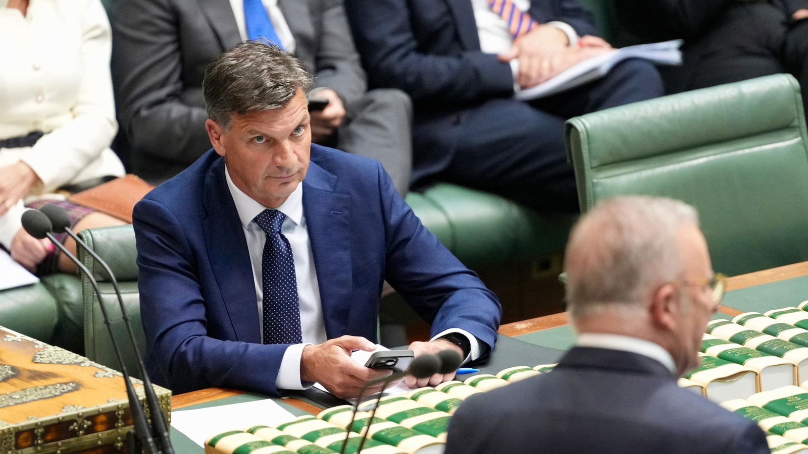 Taylor holds his phone and looks at Albanese while sitting