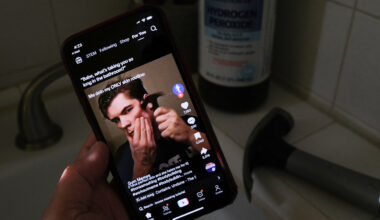 A person is holding up a phone depicting a man holding a hammer to his face in a dark bathroom.