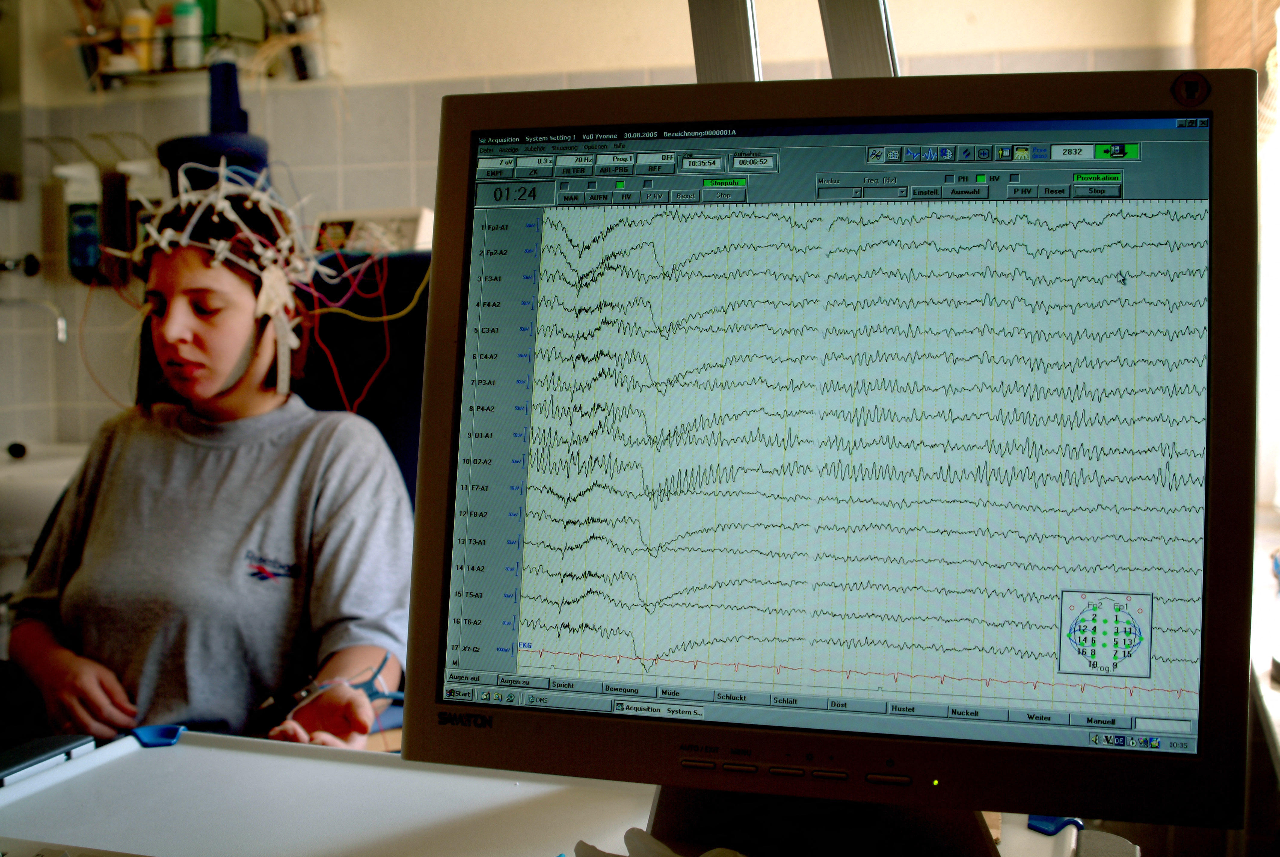 A child with a wired headset sits behind a computer display with various waves on it.