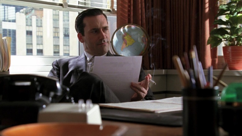 Don Draper sitting at his desk and looking up from a sheet of paper on Mad Men S1E12