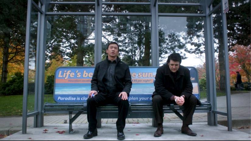 Two young men sit on a bench at a bus stop, one holding a glowing vial and one with a bandage over his hand in the Fringe episode "Making Angels"