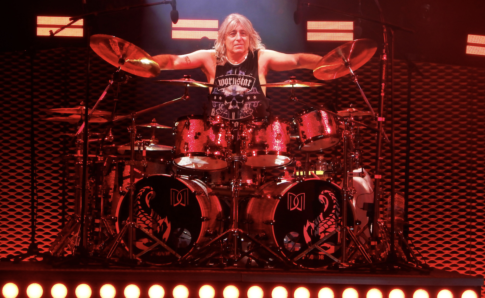 Mikkey Dee playing drums on stage during a live Scorpions concert, with stage lighting and the audience in the background.