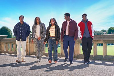 A group of young people stand together on a clear day (Myles, Sekou, Jodie, Aruna, Josh from the TV show Boarders). 