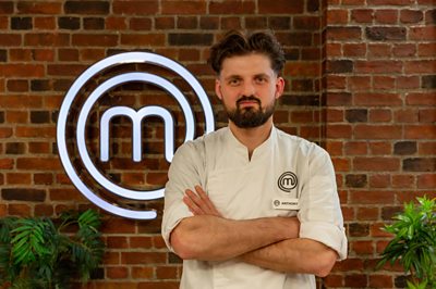 A chef poses in the MasterChef studio with an ANTHONY name badge.