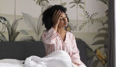 Woman sitting up in bed with her palm on her forehead and her eyes closed