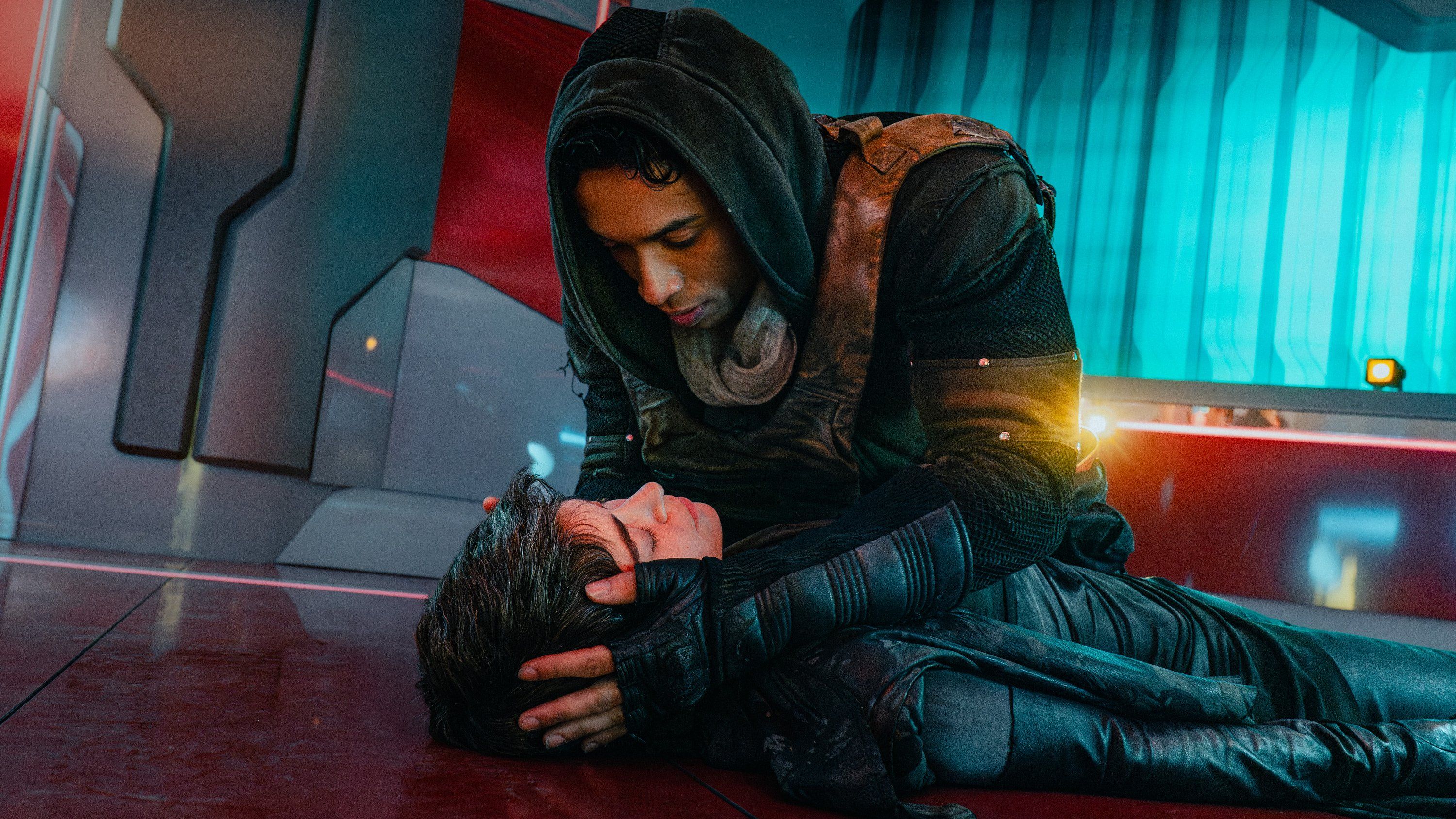 Caleb Mir (Sandro Rosta) kneels down and holds the head of his unconscious mother Anisha (Tatiana Maslany) in Starfleet Academy