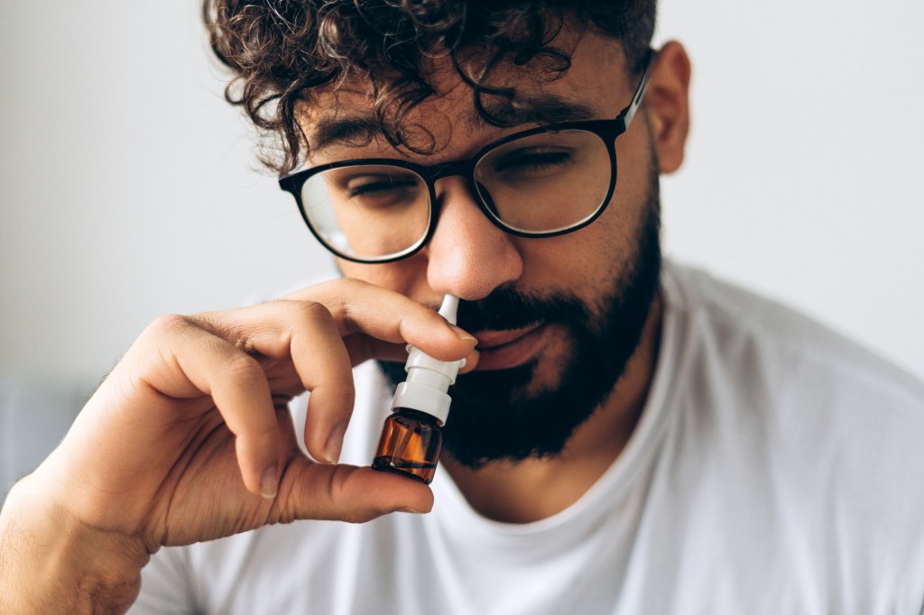 Close-up of a sick Middle Eastern man with glasses using a nasal spray.