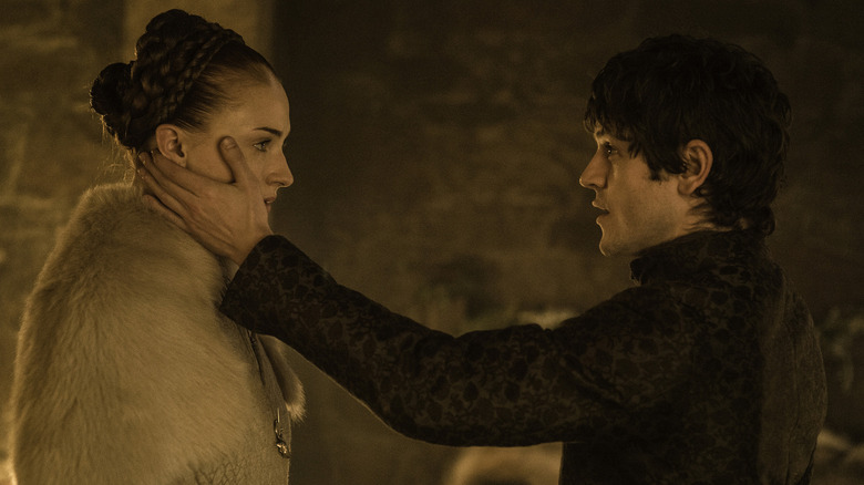 Iwan Rheon as Ramsay Bolton caressing Sophie Turner as Sansa Stark in a dimly-lit room in Game of Thrones